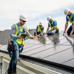 Certified workers inspecting a residential roof covered with dark tempered-glass solar roof tiles during a professional Tesla Solar Roof installation.